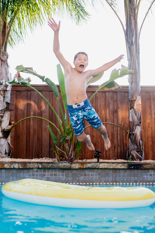 Portrait Of Shirtless Boy Jumping In Swimming Pool Against Clear Sky During Sunset
